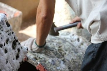 a man hammering stone pottery to create craters for the bubble glaze